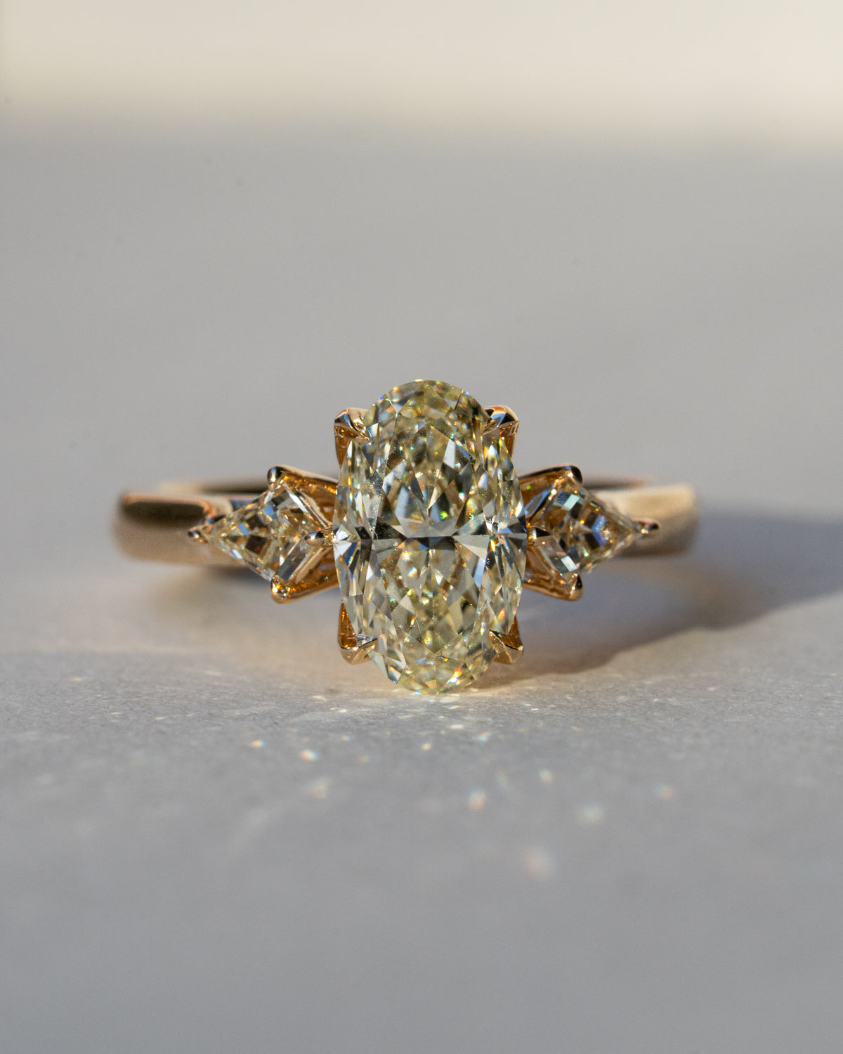 Natural oval diamond three-stone engagement ring in 18k yellow gold with custom kite side stones, front view close-up