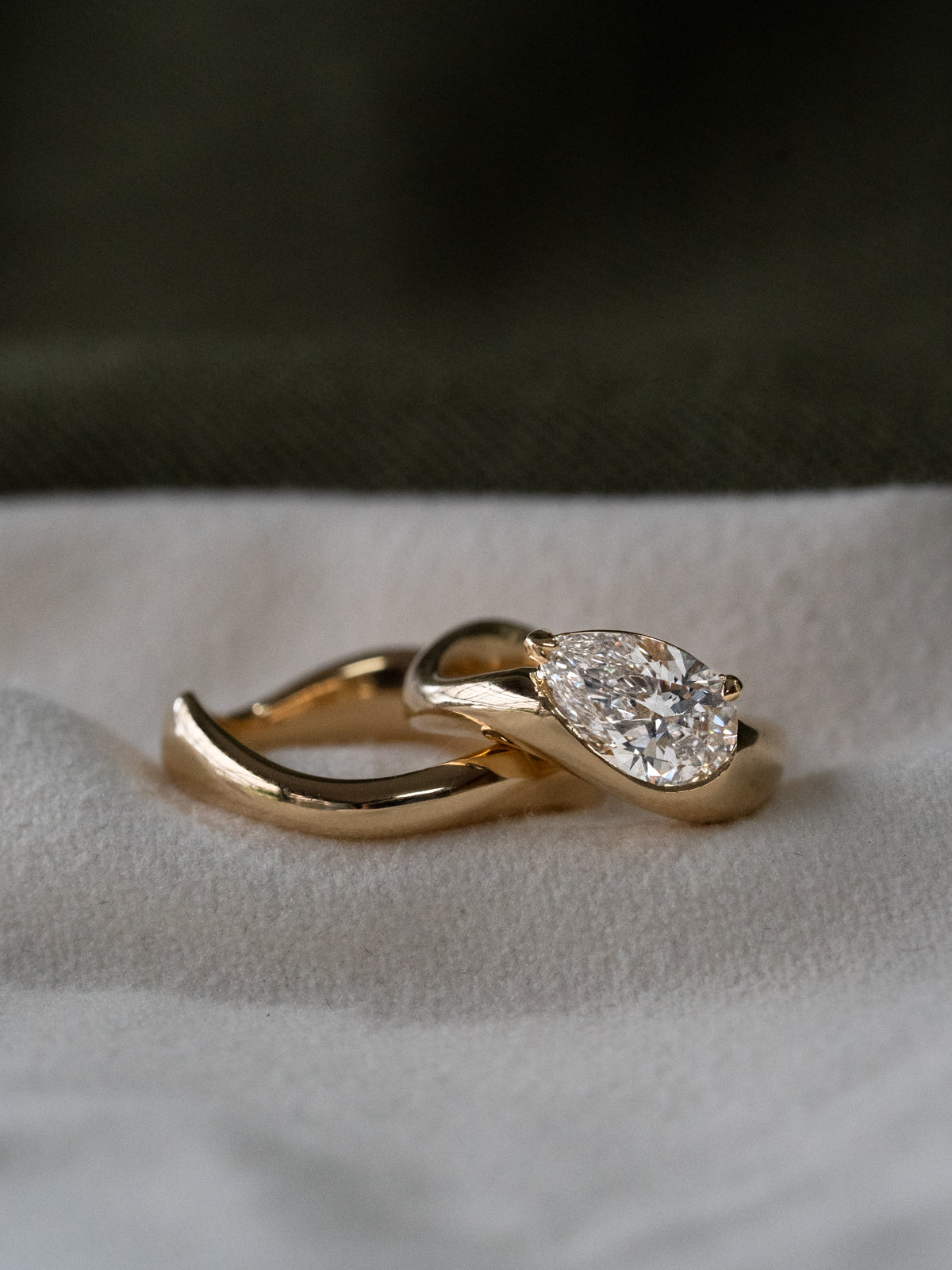 ALT TEXT FOR IMAGE 1:
"Close-up of a pear-cut diamond engagement ring in 18k yellow gold, featuring a large brilliant diamond set in a sculptural flowing setting, shown on a person's finger with sparkly nail polish against a dark background.