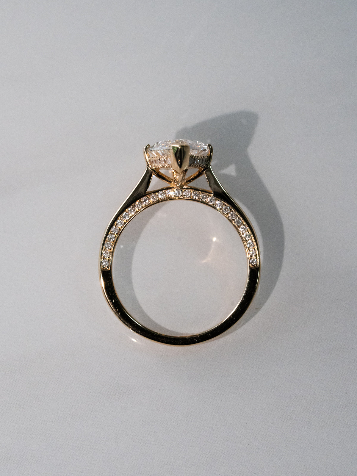 Side view of marquise diamond engagement ring showing cathedral setting and pavé diamond band in yellow gold