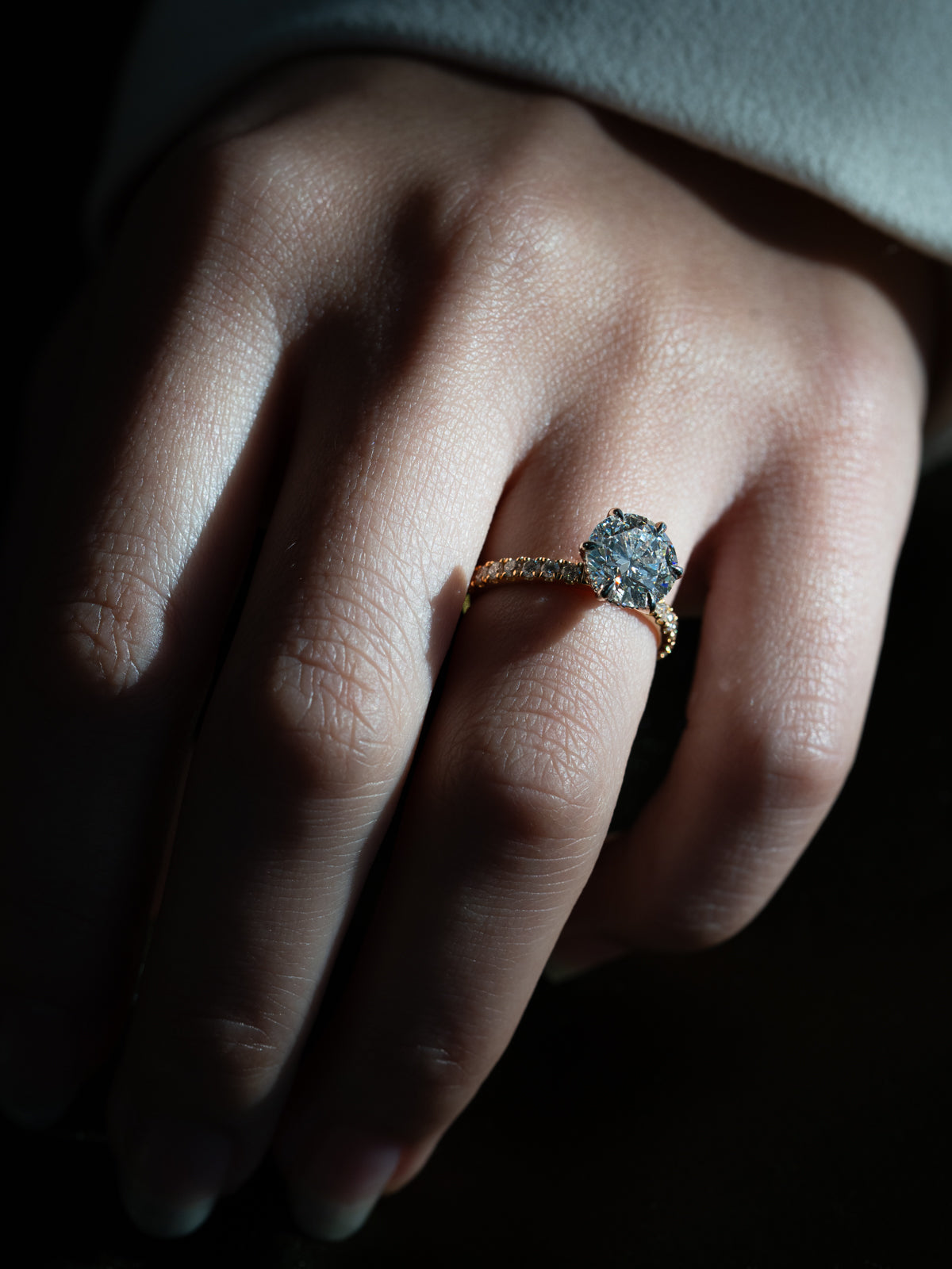 Round diamond solitaire engagement ring on hand showing 2.3ct diamond in platinum setting with yellow gold pavé band