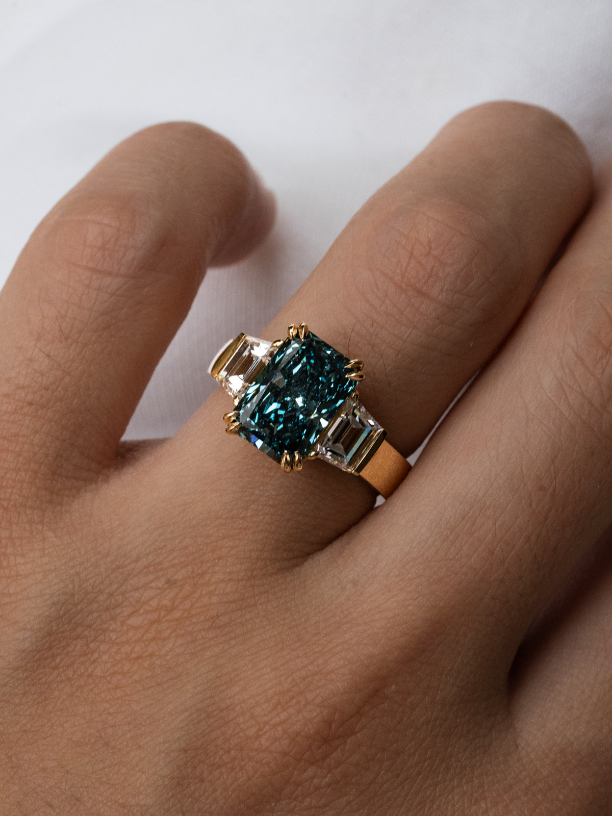 Top-down view of blue radiant cut diamond ring in 18k yellow gold showing trapezoid side stone setting detail