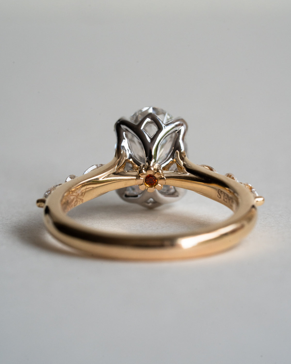 Oval diamond ring showing hidden red garnet daisy beneath floral basket setting