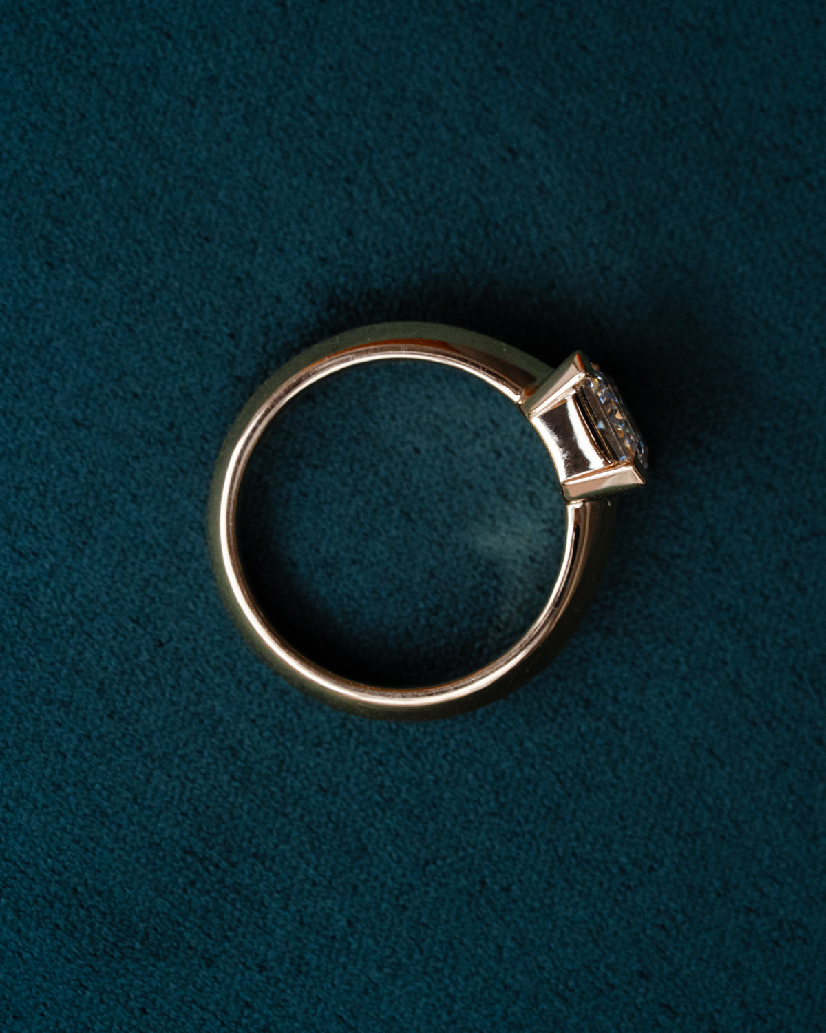 Custom yellow gold engagement ring with emerald cut diamond on hand, showing modern half bezel setting