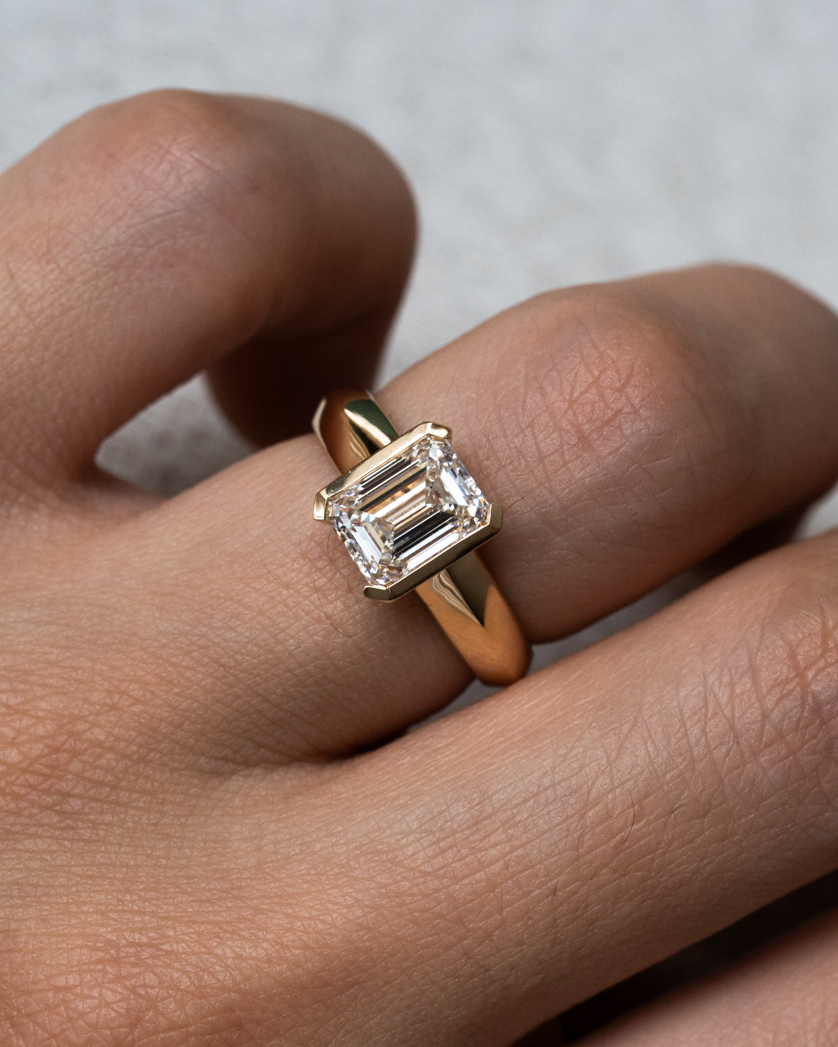 Bold yellow gold engagement ring featuring emerald cut diamond in half bezel setting, custom design