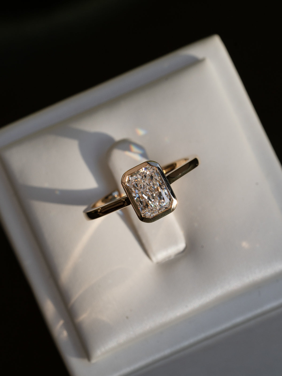 Gold ring with a diamond on a white cushion against a black background