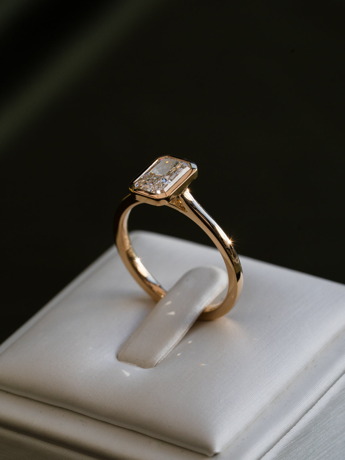 Gold bezel ring with a diamond on a white box against a dark background