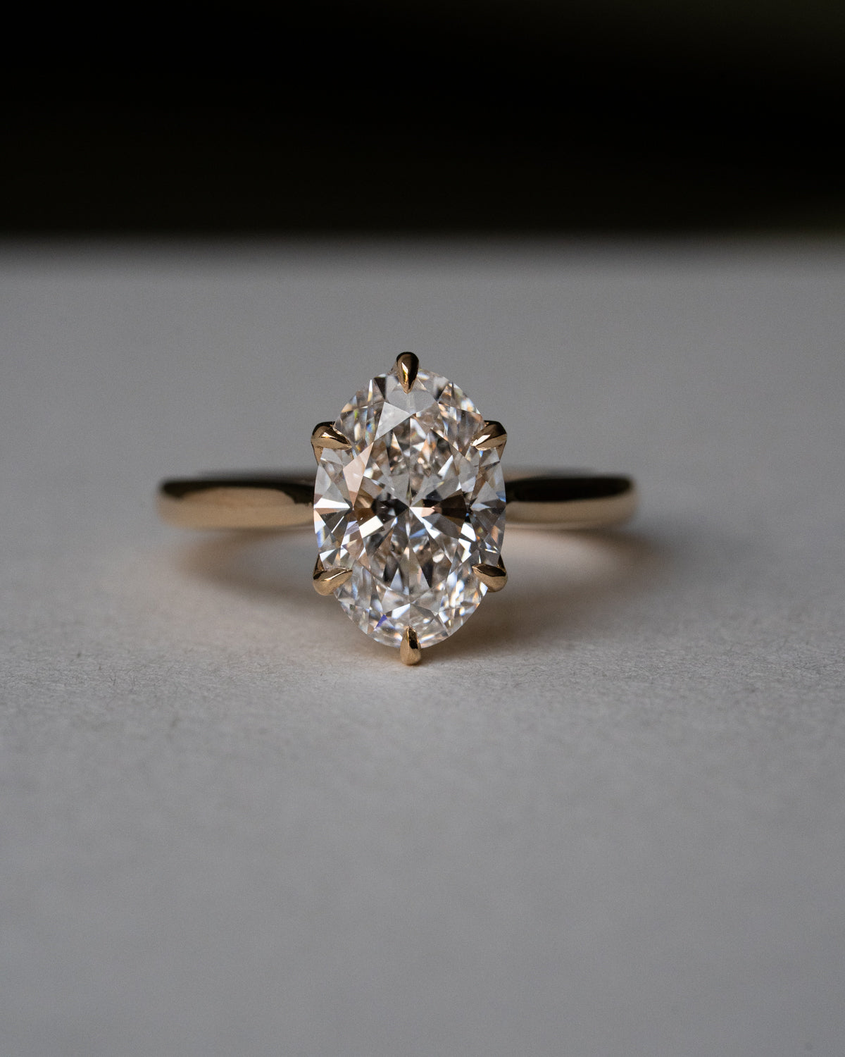 Custom oval cut diamond engagement ring with overlapping floral prongs in yellow gold, side view showing pavé set bridge and unique sculptural setting