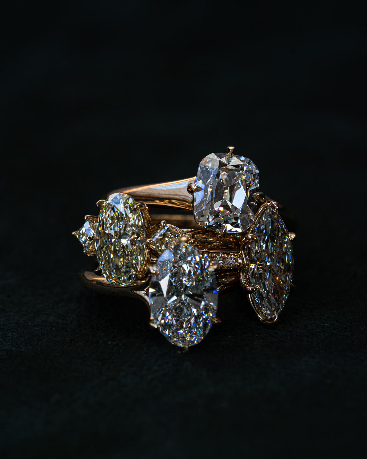 A luxury 18k yellow gold ring featuring multiple brilliant-cut diamonds in a cluster setting, photographed on a dark textured background.